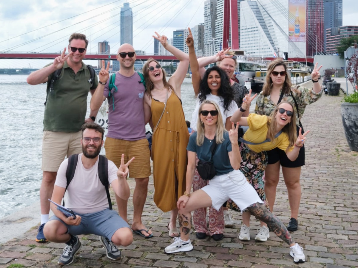 Voor de Erasmusbrug staat een groep die allemaal met hun wijs en middelvinger het peace teken uitbeelden